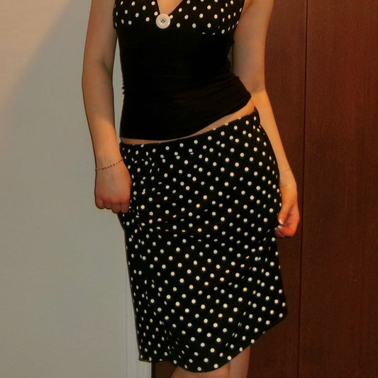 Person wearing a black polka dot top and skirt against a neutral background